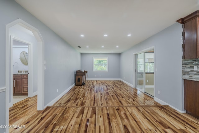 unfurnished living room with recessed lighting, baseboards, a sink, and light wood finished floors