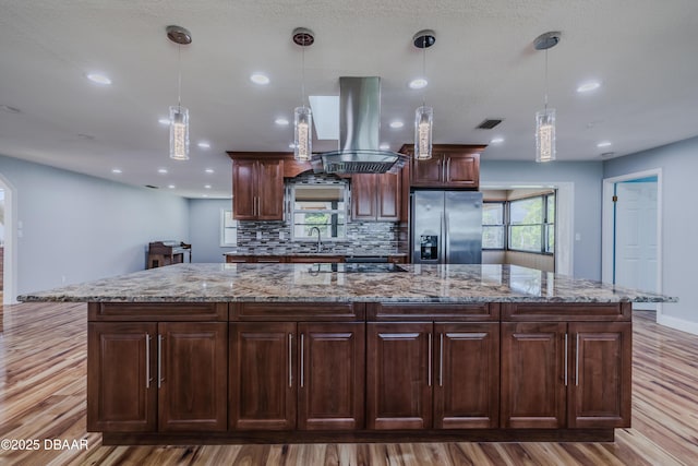 kitchen with a spacious island, island exhaust hood, a sink, decorative backsplash, and stainless steel fridge