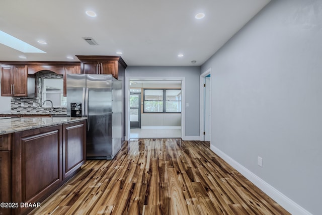 kitchen featuring visible vents, stainless steel refrigerator with ice dispenser, a skylight, decorative backsplash, and baseboards