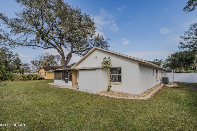 rear view of house featuring stucco siding, fence, cooling unit, a yard, and a sunroom