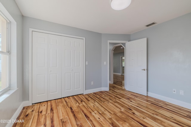 unfurnished bedroom with a closet, visible vents, light wood-style flooring, and arched walkways