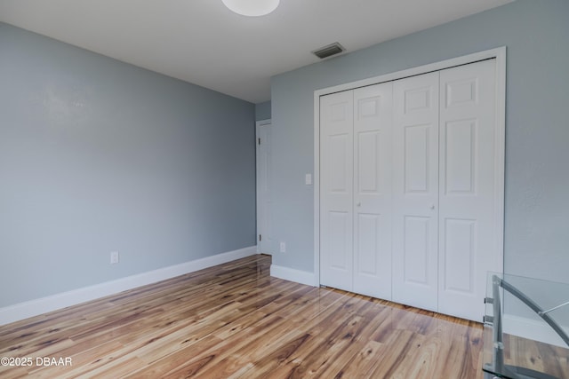 unfurnished bedroom with a closet, visible vents, light wood-type flooring, and baseboards