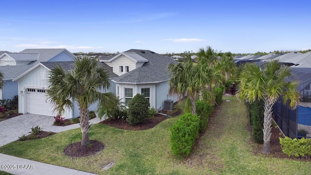 view of front facade featuring a front yard, central AC, roof with shingles, decorative driveway, and a garage