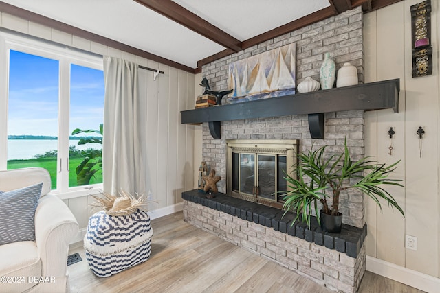 living room with beamed ceiling, light wood-type flooring, a water view, and a fireplace