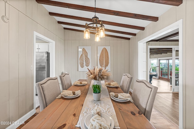 dining room featuring lofted ceiling with beams, light hardwood / wood-style floors, a notable chandelier, and wooden walls