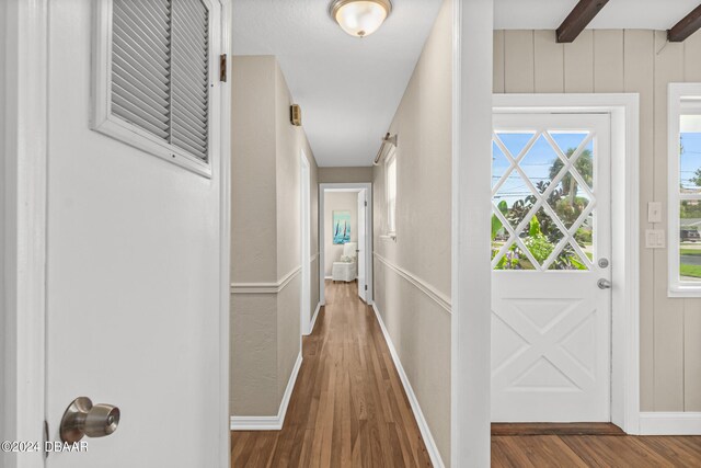 corridor featuring wood walls, dark wood-type flooring, and beamed ceiling