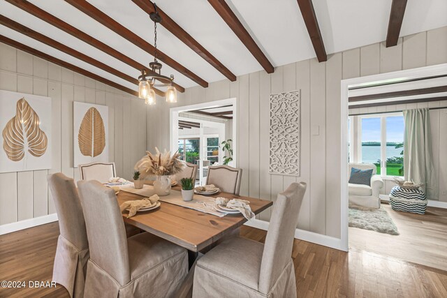 dining room with an inviting chandelier, dark hardwood / wood-style floors, a water view, and vaulted ceiling with beams