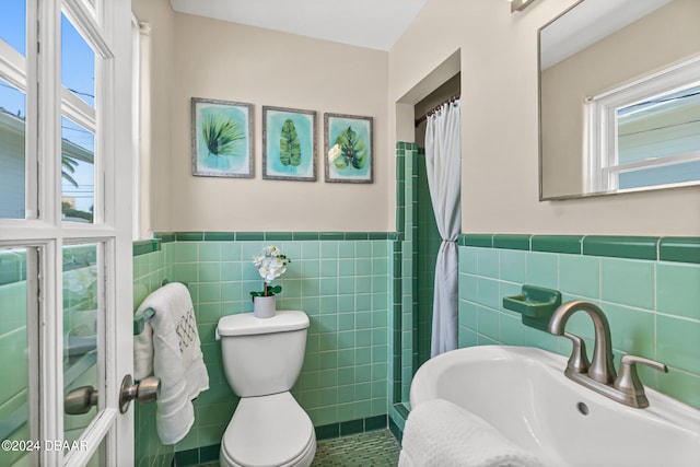 bathroom with toilet, a shower with curtain, tile walls, and sink