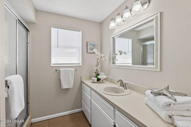 bathroom featuring walk in shower, vanity, a textured ceiling, and tile patterned flooring