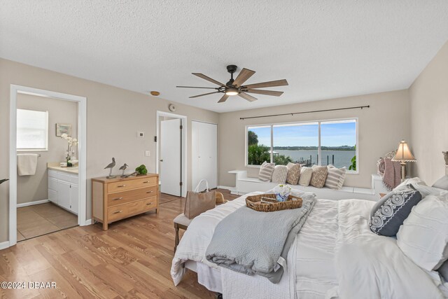 bedroom with a water view, ceiling fan, a textured ceiling, light hardwood / wood-style flooring, and connected bathroom