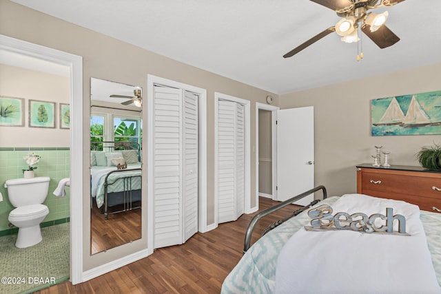 bedroom featuring tile walls, connected bathroom, dark wood-type flooring, two closets, and ceiling fan