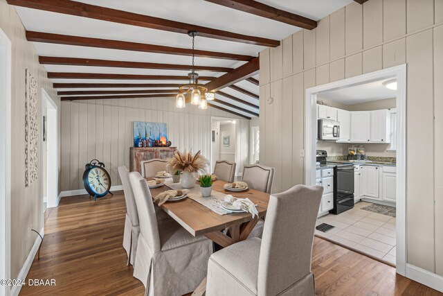 dining space featuring hardwood / wood-style floors, lofted ceiling with beams, wooden walls, and a notable chandelier