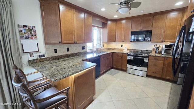 kitchen with black appliances, a sink, dark stone countertops, a peninsula, and brown cabinetry