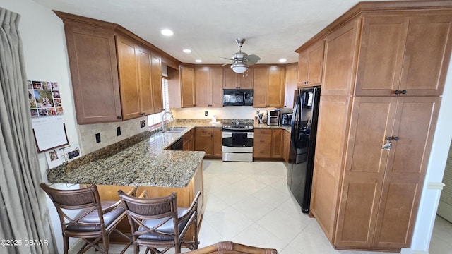 kitchen featuring a peninsula, brown cabinetry, stone countertops, black appliances, and a sink