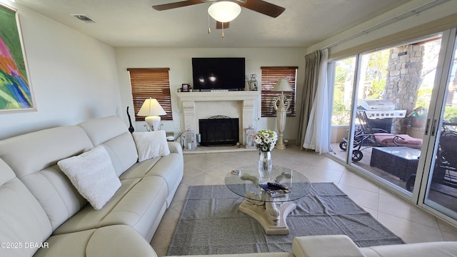 living room featuring light tile patterned floors, visible vents, a fireplace with raised hearth, and a ceiling fan