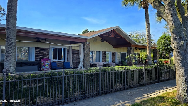 view of front of property featuring stone siding, fence private yard, and a ceiling fan