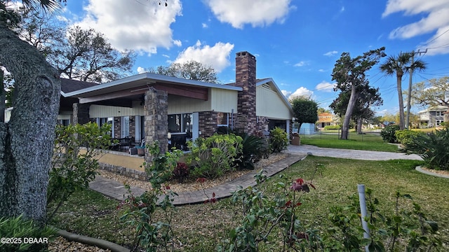 view of home's exterior with brick siding, a lawn, a chimney, and fence