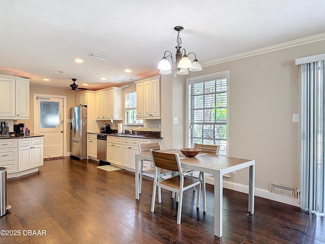 dining area with ceiling fan with notable chandelier, sink, crown molding, and dark wood-type flooring