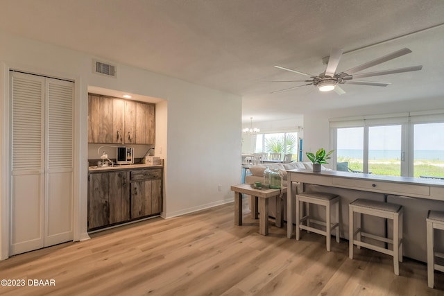 kitchen featuring sink, ceiling fan with notable chandelier, a kitchen breakfast bar, and light hardwood / wood-style flooring