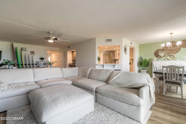 living room with ceiling fan with notable chandelier and light hardwood / wood-style flooring