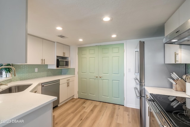 kitchen with stainless steel appliances, light hardwood / wood-style floors, white cabinetry, sink, and wall chimney exhaust hood