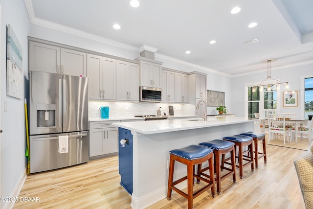 kitchen with a kitchen breakfast bar, gray cabinets, stainless steel appliances, and an island with sink