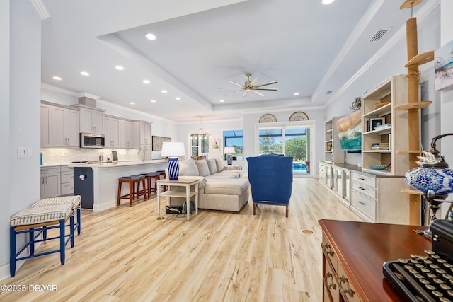 living room with light hardwood / wood-style flooring, sink, ceiling fan, crown molding, and a raised ceiling