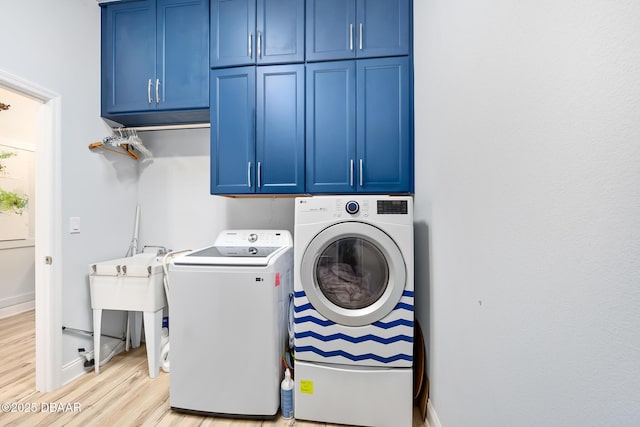 clothes washing area with cabinets, separate washer and dryer, sink, and light wood-type flooring