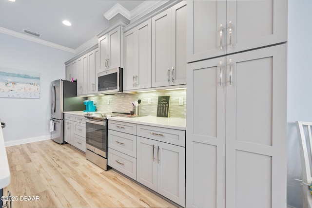 kitchen featuring appliances with stainless steel finishes, crown molding, decorative backsplash, and light hardwood / wood-style flooring