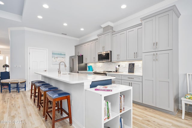 kitchen with a kitchen breakfast bar, a kitchen island with sink, gray cabinetry, and stainless steel appliances