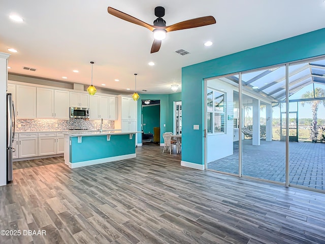 kitchen with decorative backsplash, stainless steel appliances, a center island with sink, white cabinetry, and hanging light fixtures