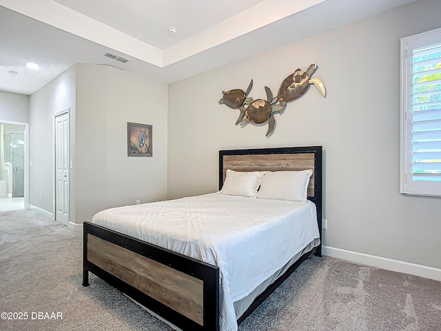 carpeted bedroom featuring ensuite bathroom, a raised ceiling, and a closet