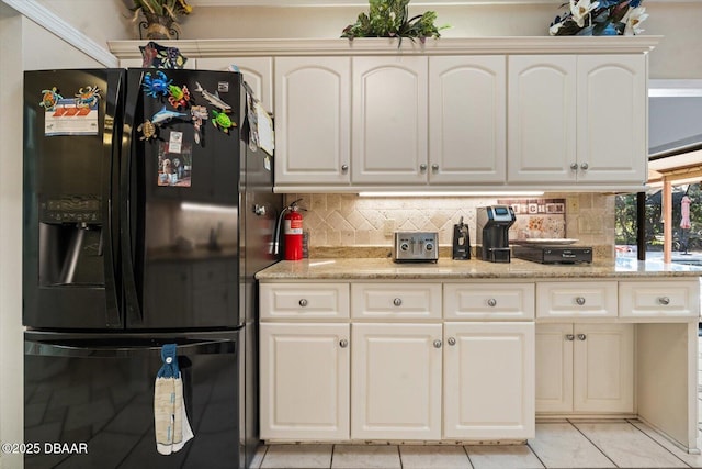 kitchen with white cabinetry, black fridge, light stone counters, decorative backsplash, and light tile patterned floors