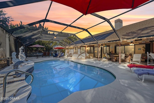 pool at dusk featuring a lanai and a patio