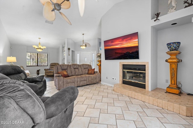 tiled living room with a fireplace, ceiling fan with notable chandelier, and vaulted ceiling