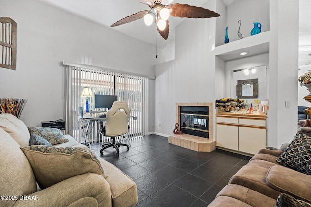 tiled living room with ceiling fan, a towering ceiling, and a tiled fireplace