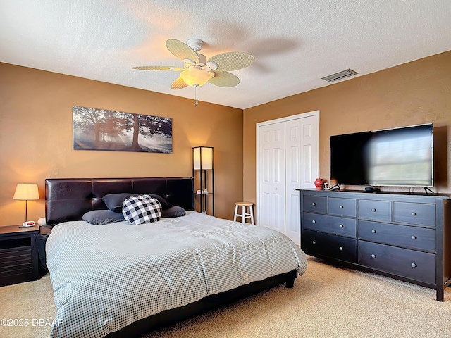 bedroom with visible vents, ceiling fan, light carpet, a closet, and a textured ceiling