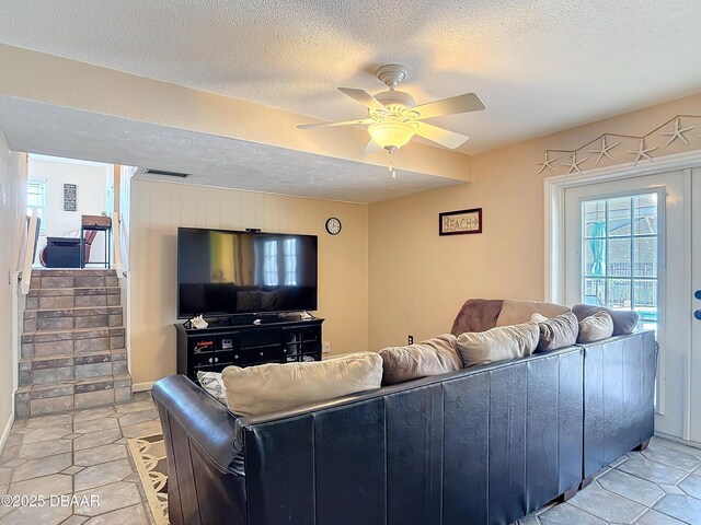 living room featuring visible vents, light tile patterned flooring, ceiling fan, stairs, and a textured ceiling