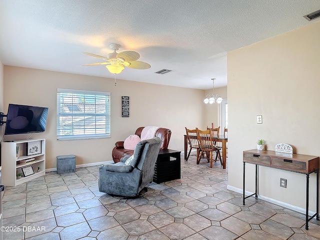 living area with baseboards, ceiling fan with notable chandelier, visible vents, and a textured ceiling