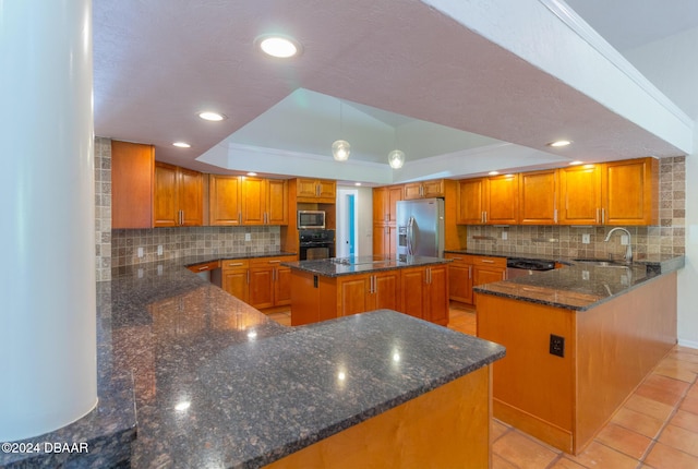 kitchen with sink, a tray ceiling, a kitchen island, kitchen peninsula, and stainless steel appliances