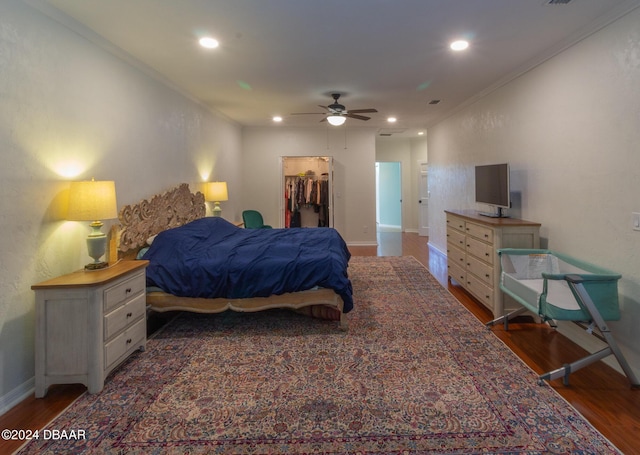 bedroom featuring a walk in closet, ceiling fan, ornamental molding, dark hardwood / wood-style flooring, and a closet