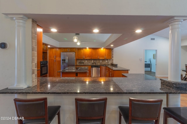 kitchen featuring kitchen peninsula, a kitchen bar, stainless steel appliances, and dark stone countertops