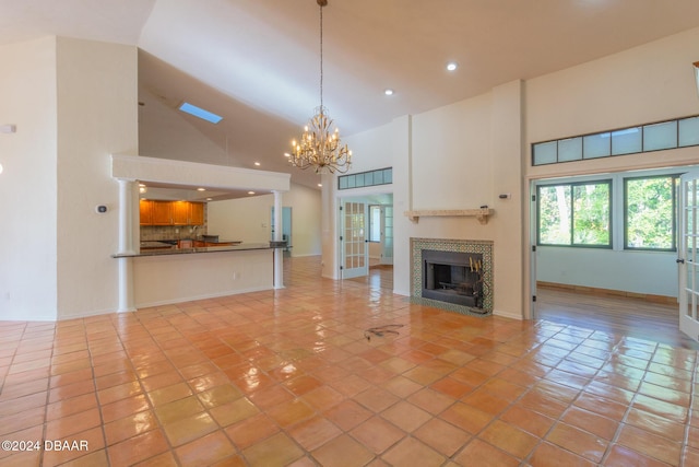 unfurnished living room with a fireplace, high vaulted ceiling, a notable chandelier, and light tile patterned flooring