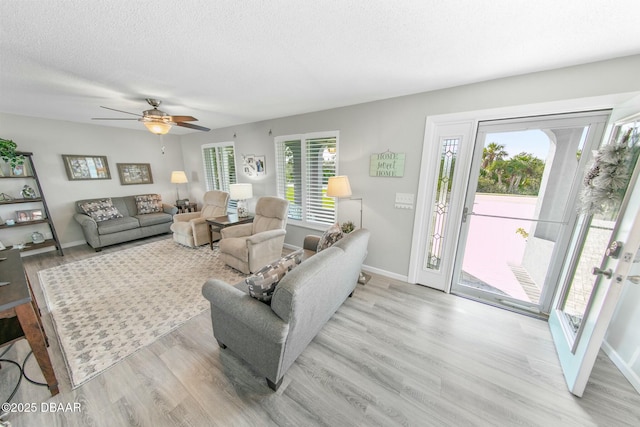 living room with ceiling fan, light wood-type flooring, and a textured ceiling