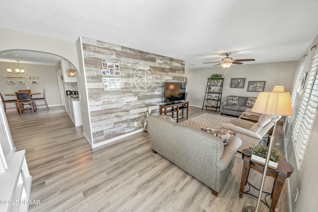 living room with a textured ceiling, light hardwood / wood-style floors, ceiling fan, and wooden walls