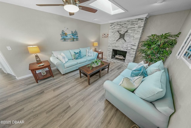 living room featuring ceiling fan, light hardwood / wood-style floors, a stone fireplace, and a skylight