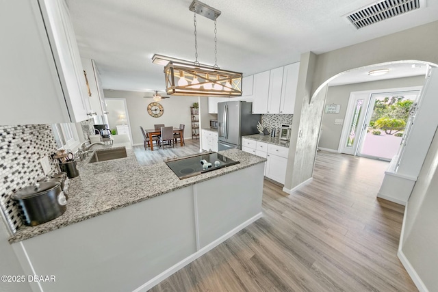 kitchen with white cabinets, stainless steel fridge, black electric stovetop, and pendant lighting