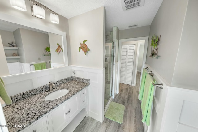 bathroom featuring a shower with shower door, vanity, wood-type flooring, and a textured ceiling