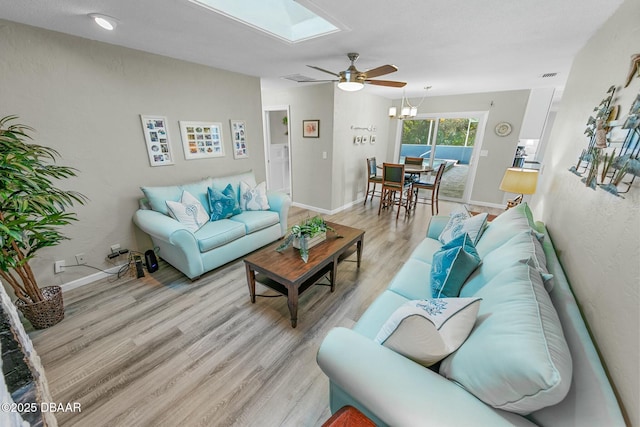 living room featuring ceiling fan, light hardwood / wood-style flooring, and a skylight