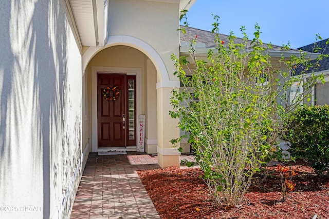 entrance to property featuring stucco siding and roof with shingles